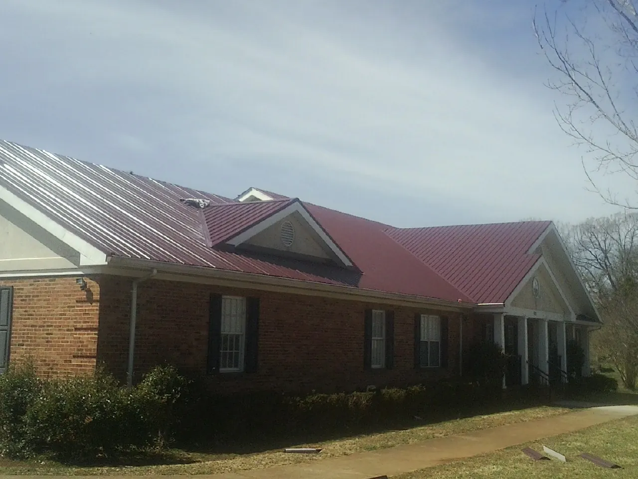Red metal roof with gabled entries on a long brick building, from a Hail Damage Roof Repair job in Hardin