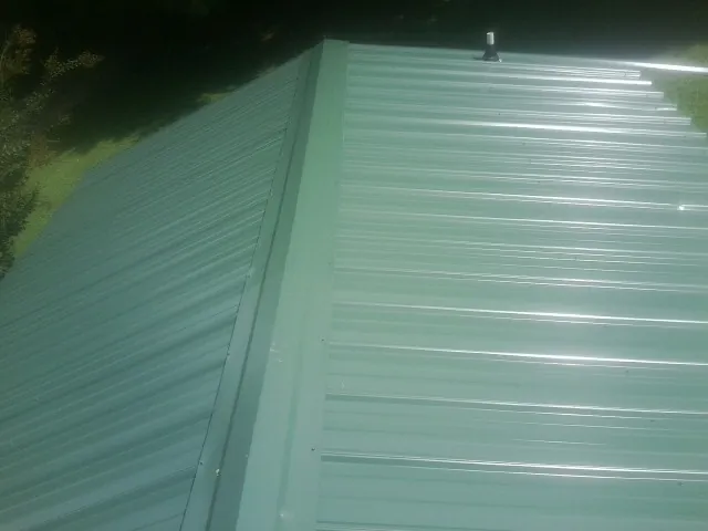 New green metal panels meeting at the ridge of a roof — Flat Roof Repair work by our crew in Hardin