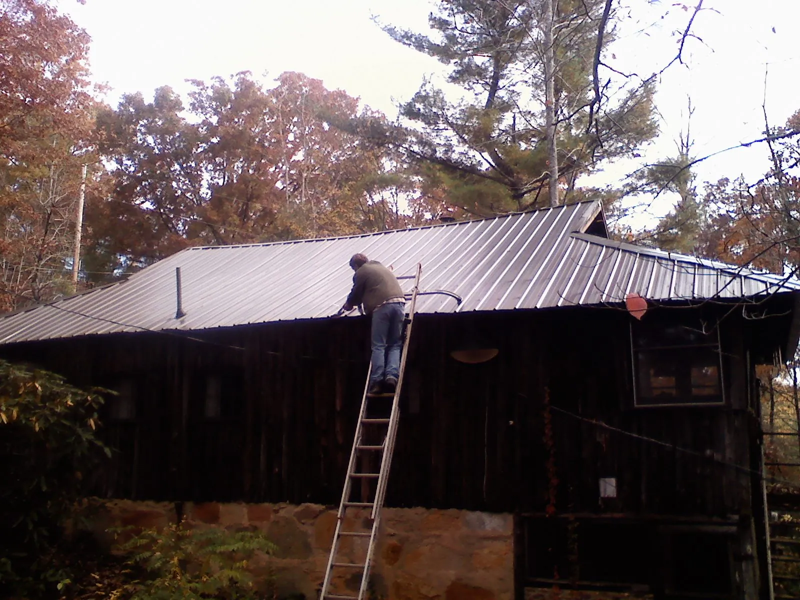 Roofer on a ladder working along the edge of a cabin metal roof in Hardin